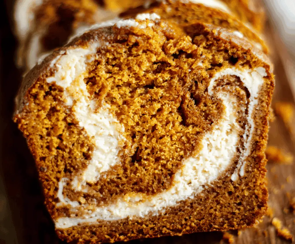 Delicious homemade pumpkin bread with a creamy cream cheese swirl topped with a cinnamon spice coating, perfect for fall baking