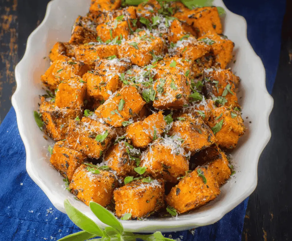Delicious roasted sweet potatoes garnished with fresh herbs and sprinkled with Parmesan cheese.