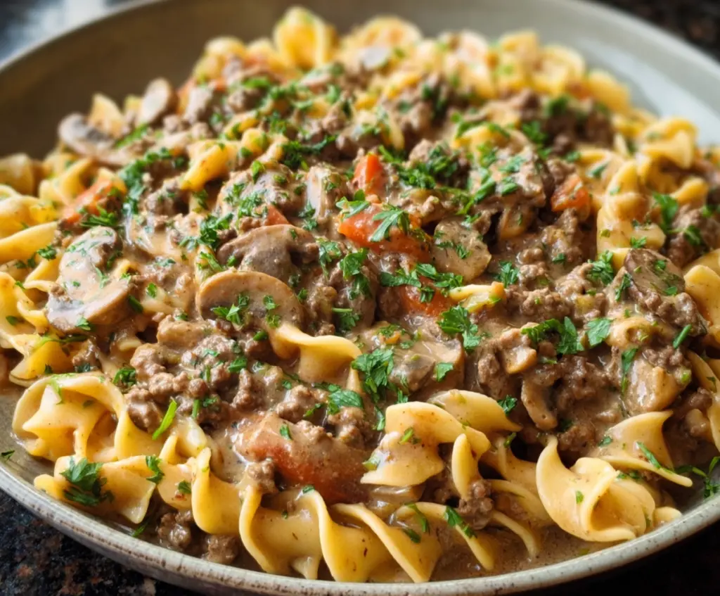 Creamy Ground Beef Stroganoff served over noodles with fresh herbs